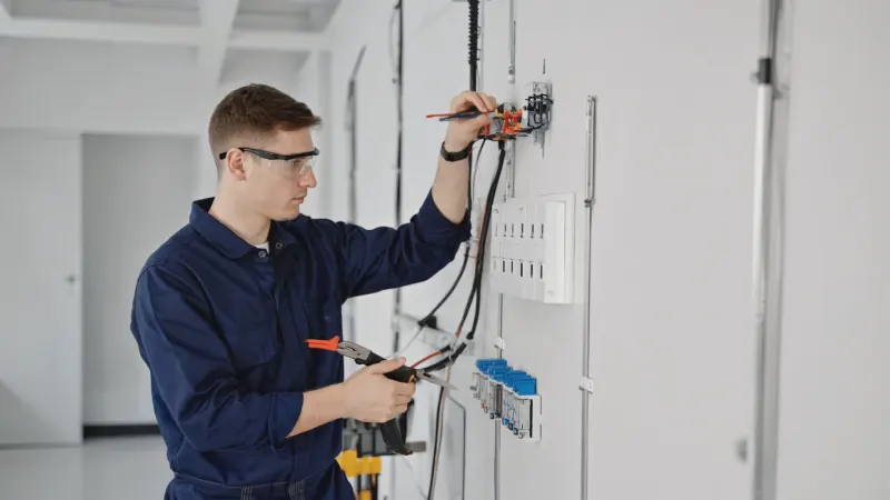 An electrician in safety glasses wiring a panel